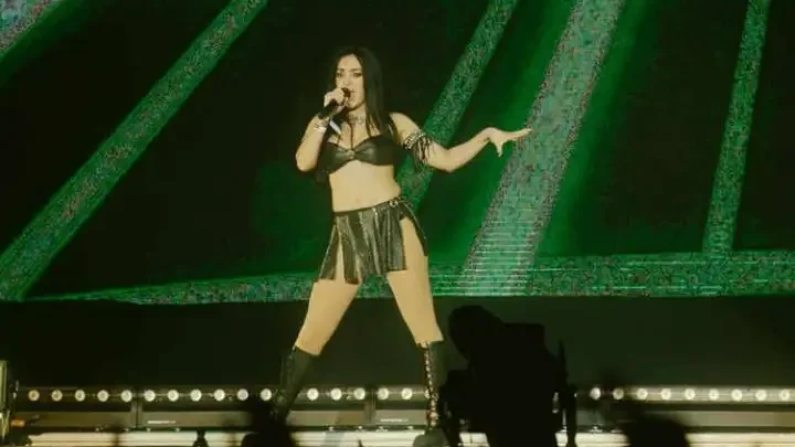 Charli xcx se apresenta no palco diante de um telão verde