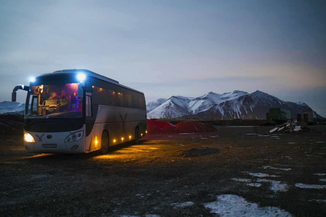 Ônibus de turismo com faróis acesos ao entardecer